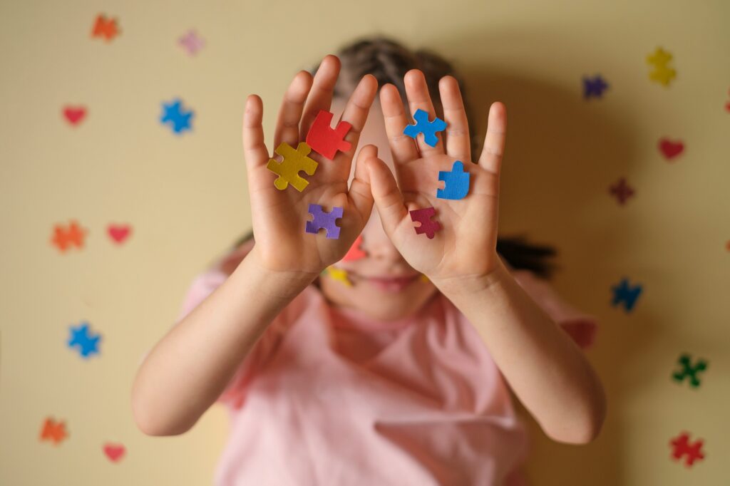A child hides face behind his hands with colorful puzzles - the emblem of autism