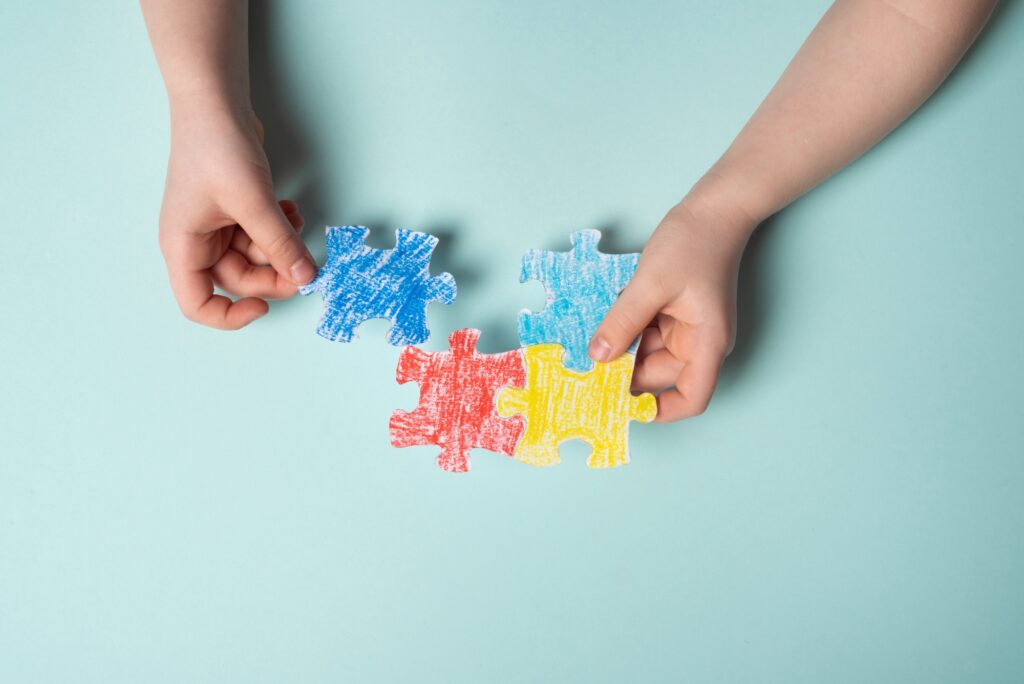 Children's hands laying out a colored puzzle, symbol of World Autism Awareness Day