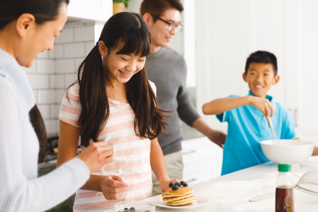 Happy asian parents with son and daughter preparing breakfast in kitchen