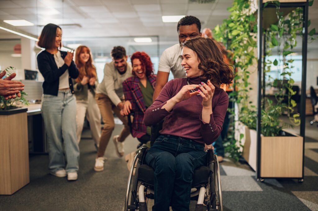 Woman who uses a wheelchair being pushed in an office chair by a black coworker