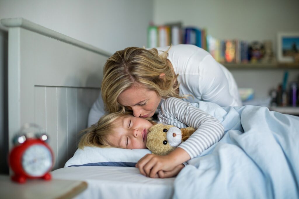 Mother kissing her daughter in the bedroom