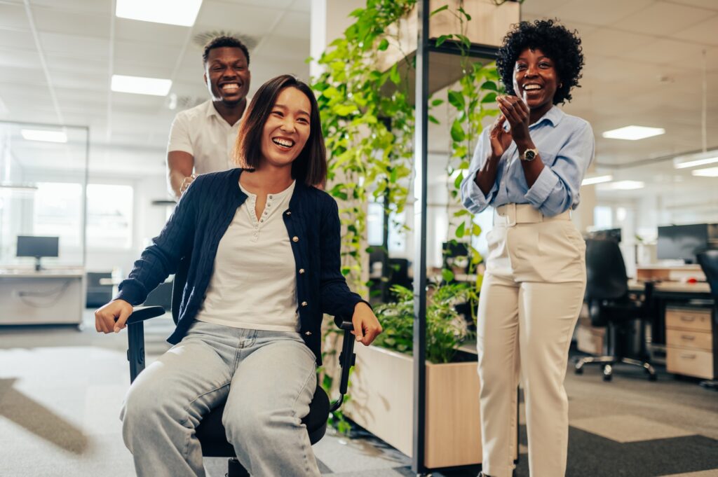 Asian woman enjoying office chair race at workspace and having fun