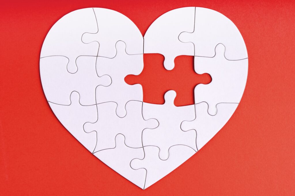 Love, charity, donation, helping concept. Missing piece of jigsaw puzzle in heart shape on red