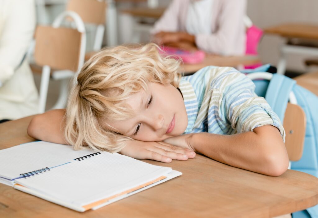 Sleepy tired bored schoolboy pupil student sleeping at the desk in school during the lesson class.