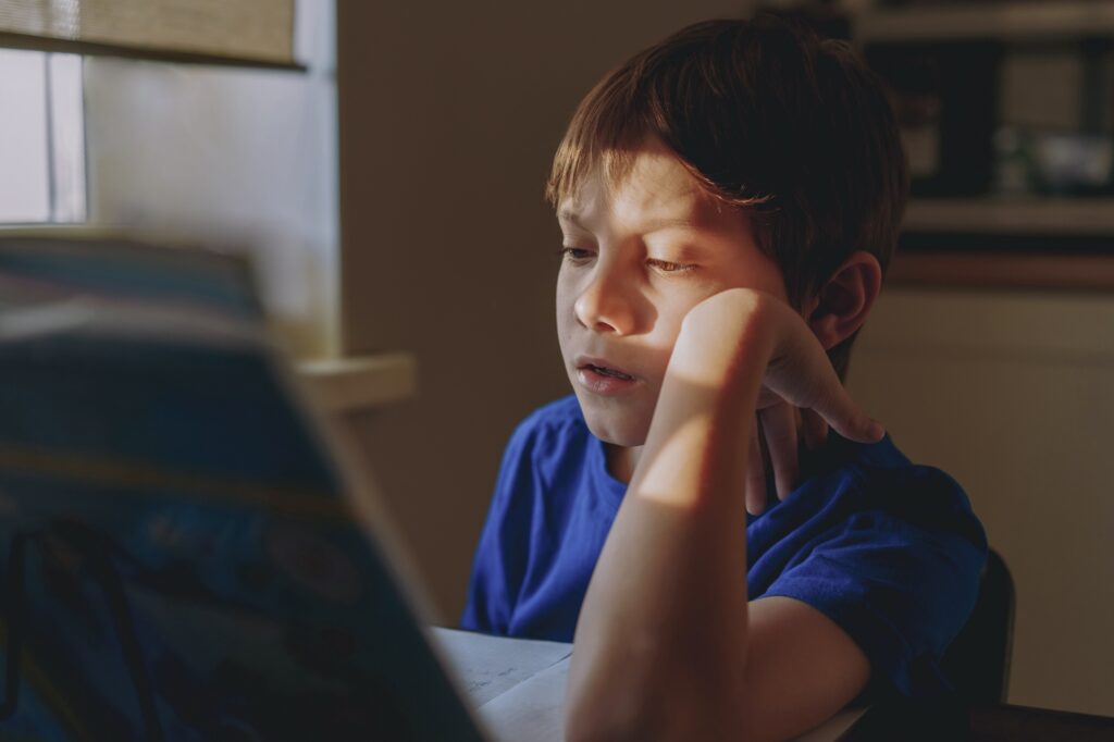 stressed tired boy doing homework at home at the desk by the window.