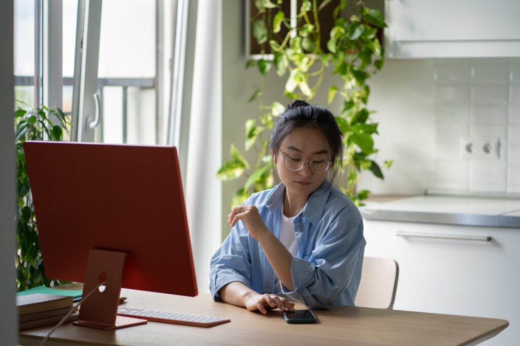 Asian student girl checking phone while studying online. Digital distractions in e-learning