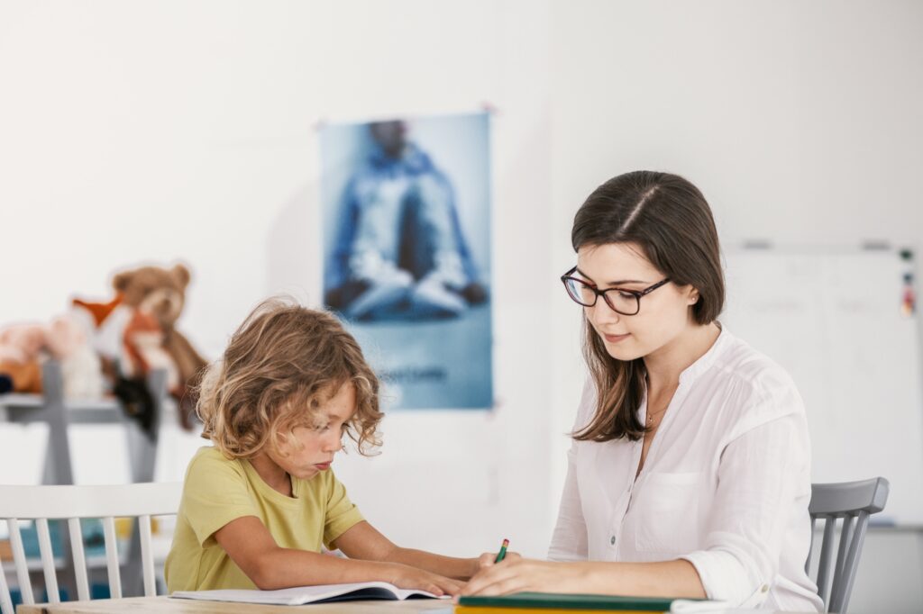 Friendly teacher doing homework with young boy in the classroom
