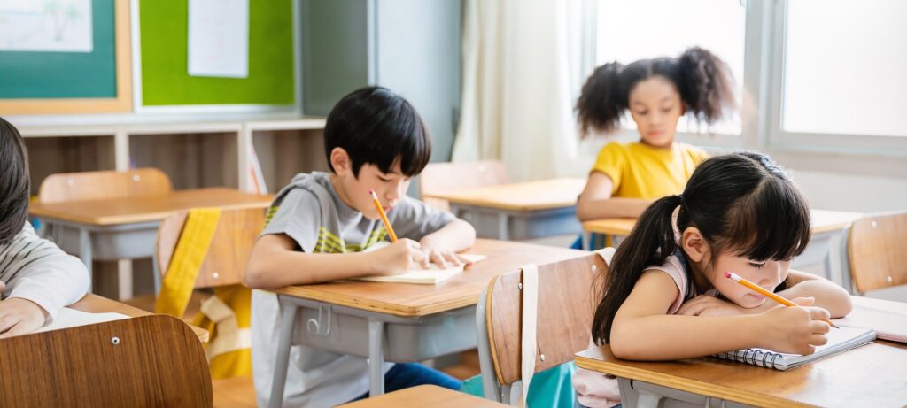 Portrait of little pupil writing at desk in classroom at the elementary school