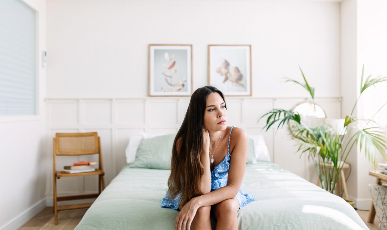 Sad young adult woman sitting on bed