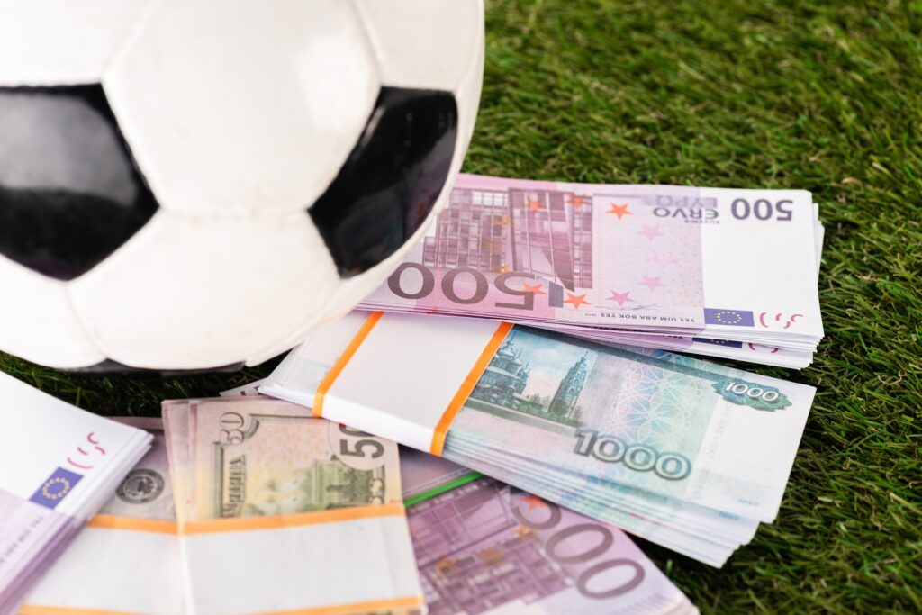 selective focus of packs of euro and dollar banknotes near soccer ball on green grass, sports