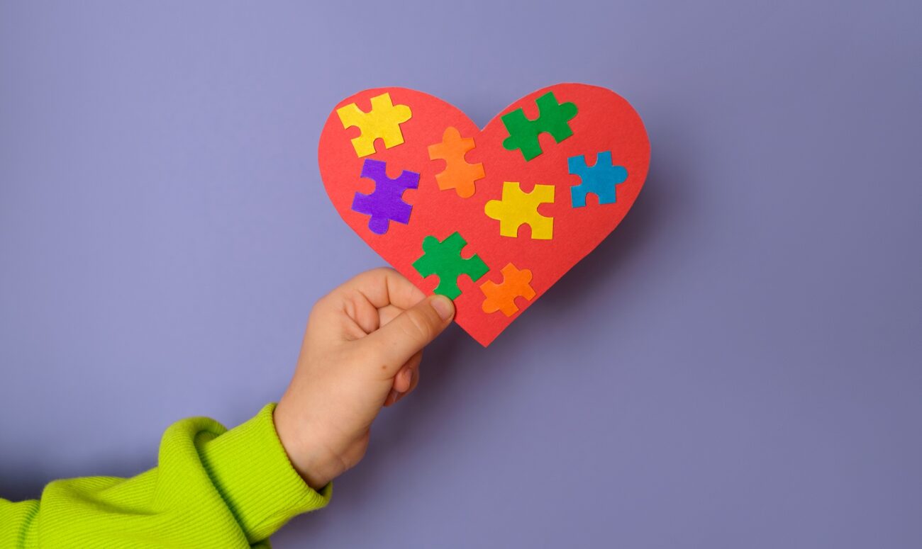 Big heart with details of puzzles in a child's hand there is a symbol of autism.
